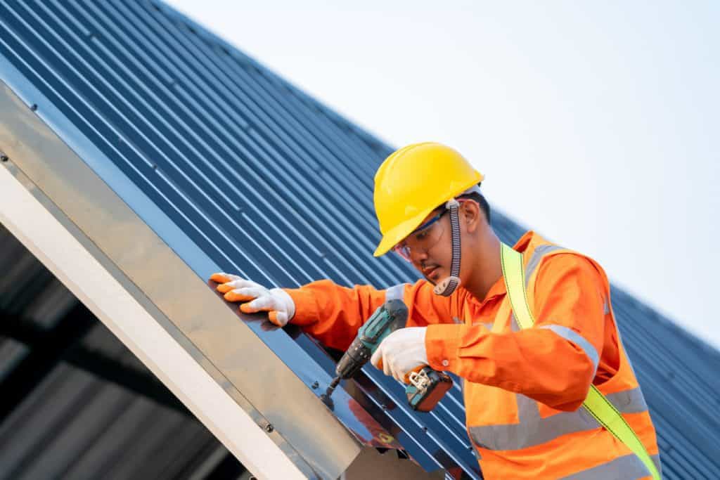 A worker uses a power drill to attach metal roofing panels, showing how Cornerstone Metals helps build strong roofs.